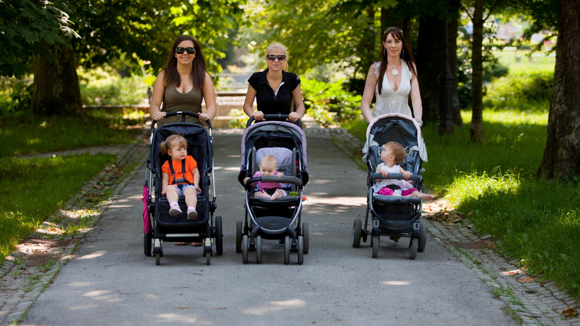 Trójka przyjaciółek, która prowadzi przez park wózki spacerowe wraz ze swoimi pociechami